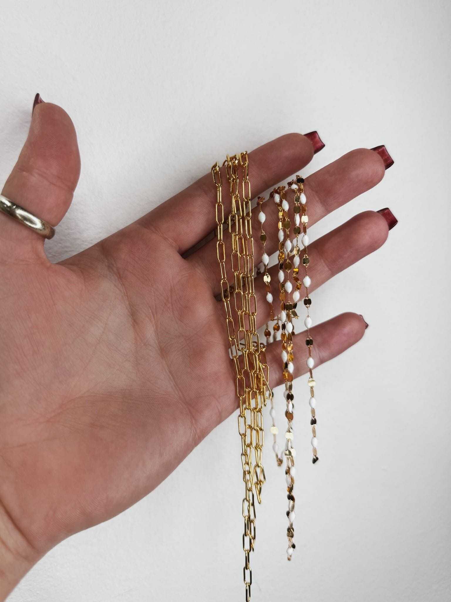 Hand displaying gold and silver chain necklaces against a white background.