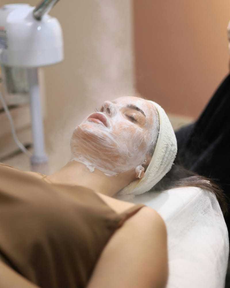 Woman receiving a facial steam treatment at a spa.