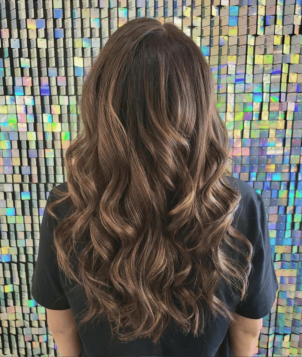 Long, wavy brown hair styled elegantly against a shimmering, colorful background.