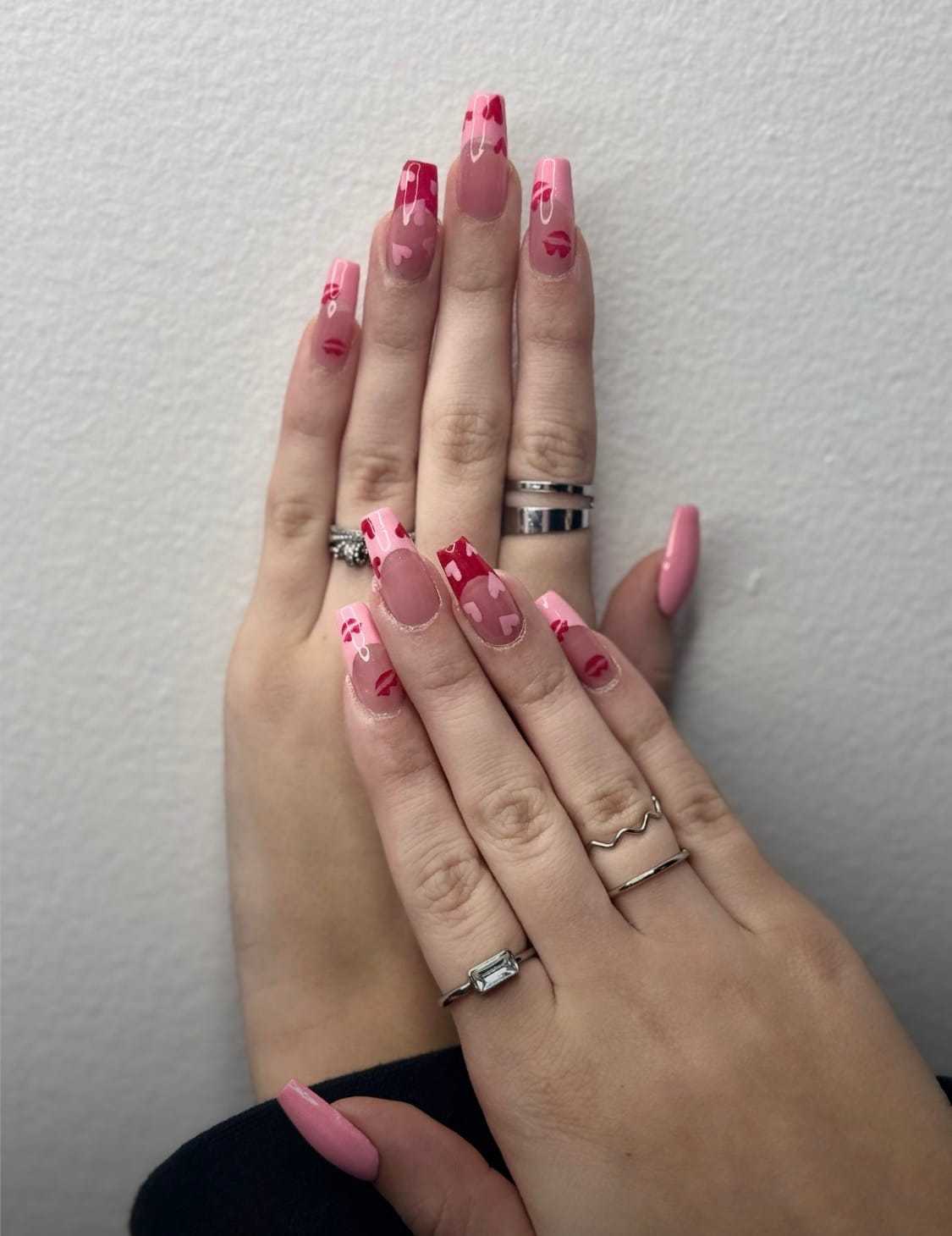 Pink manicured hands with heart designs and various rings on fingers.