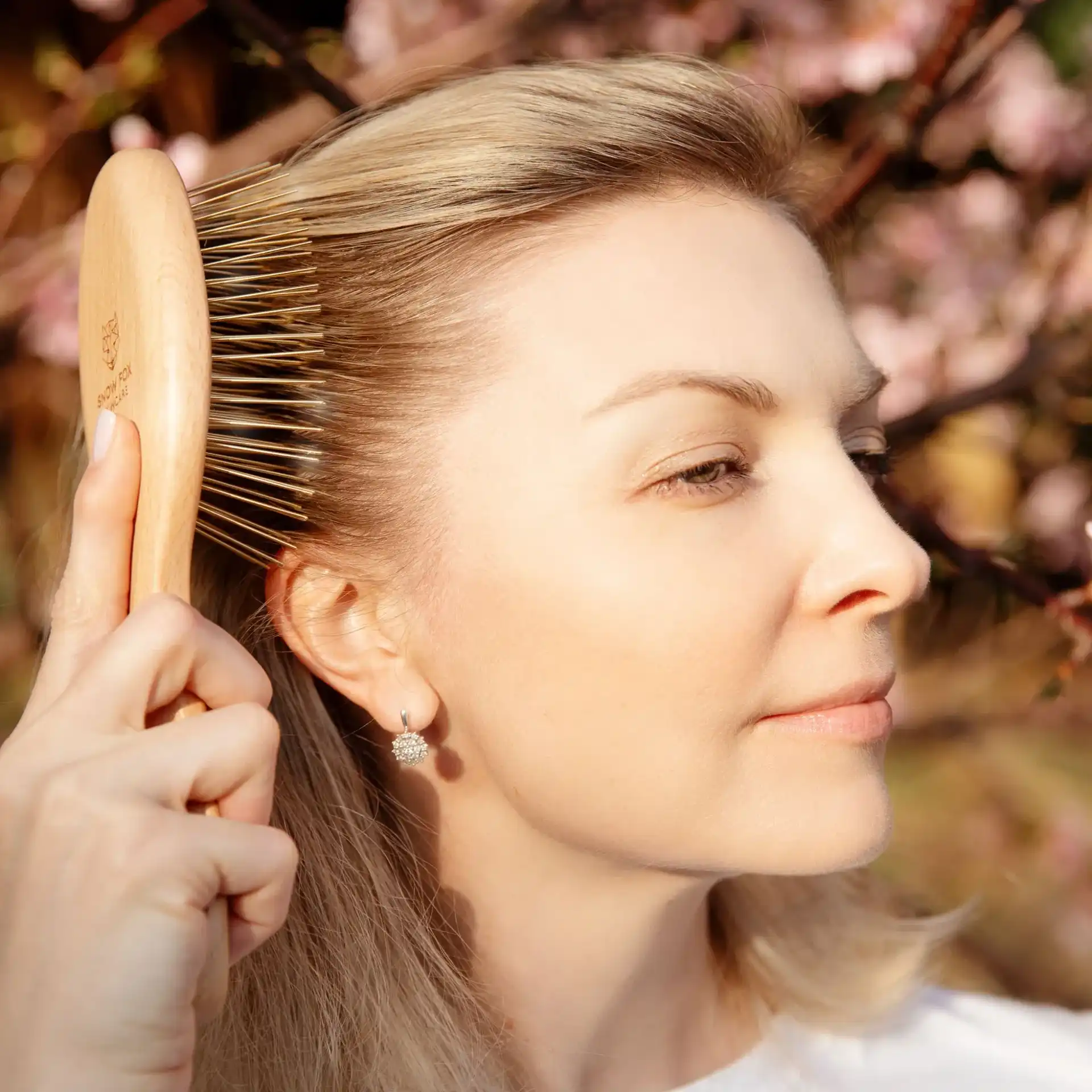 Woman brushing hair outdoors near flowering branches.