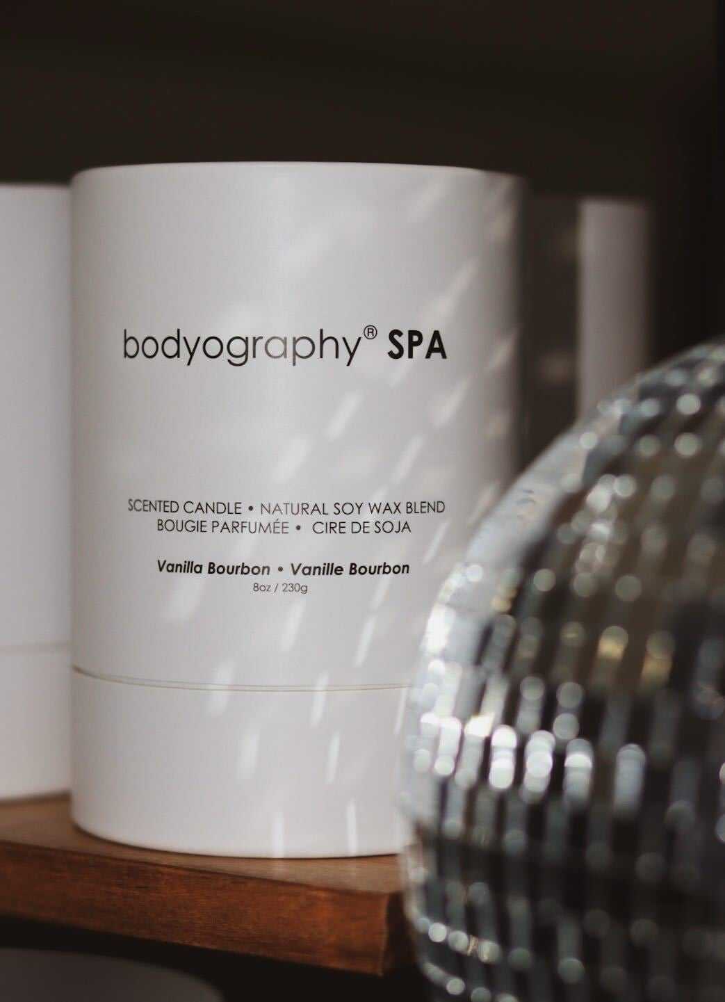 Bodyography SPA vanilla bourbon scented candle on a shelf, with a disco ball nearby.