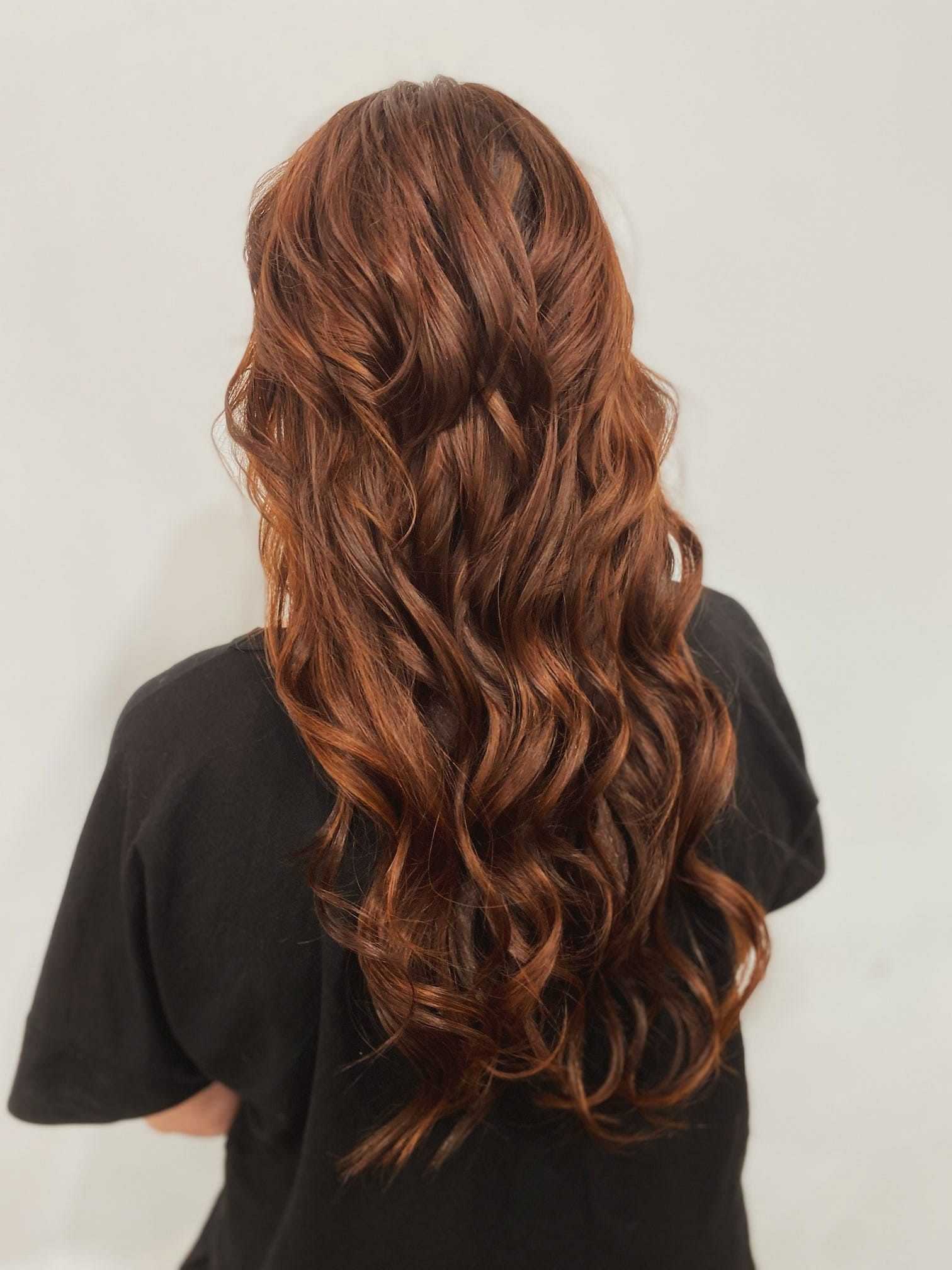 Long, wavy, auburn hair cascading down the back against a plain background.