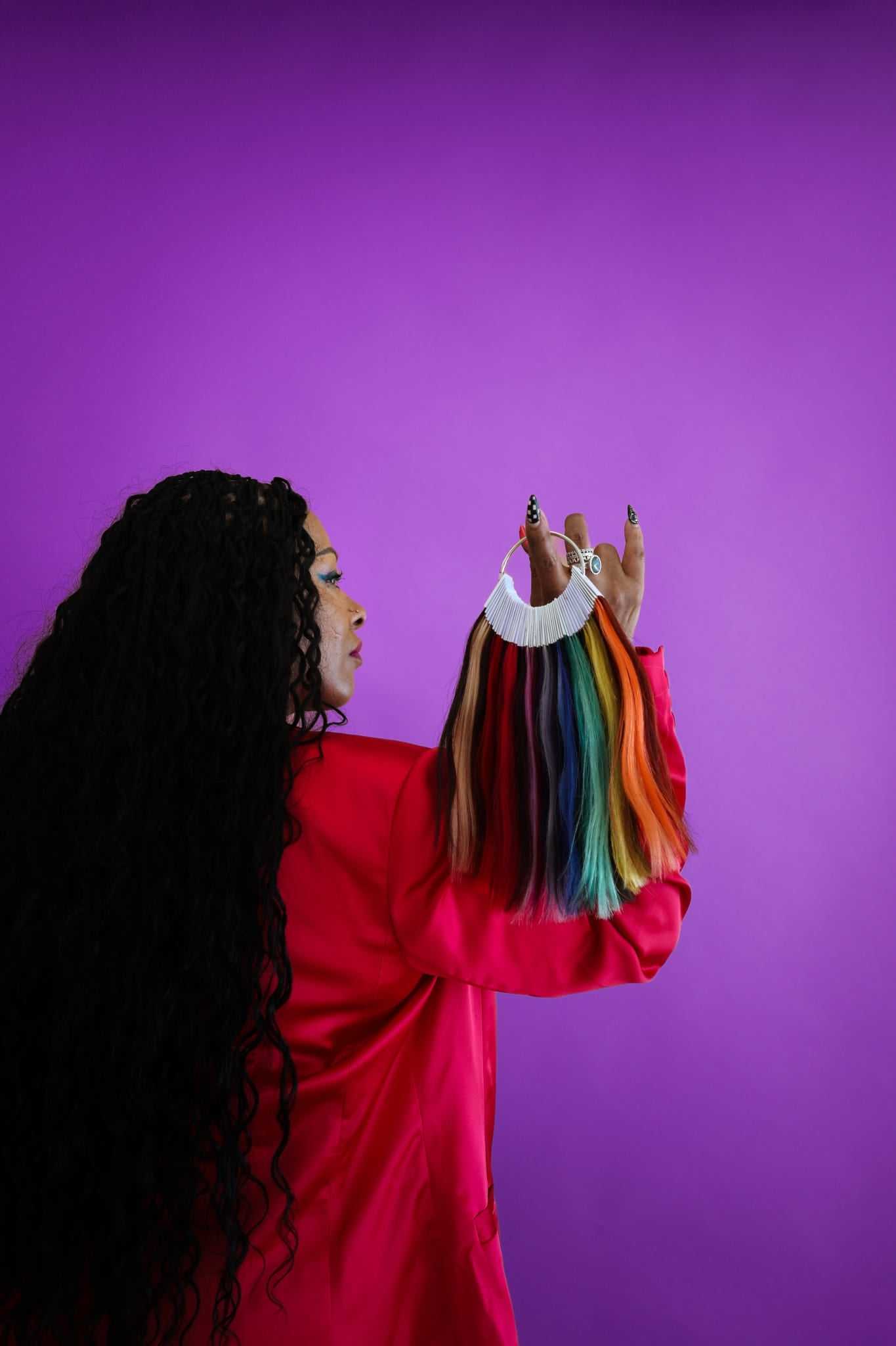 Woman holding multicolored hair samples against purple background.