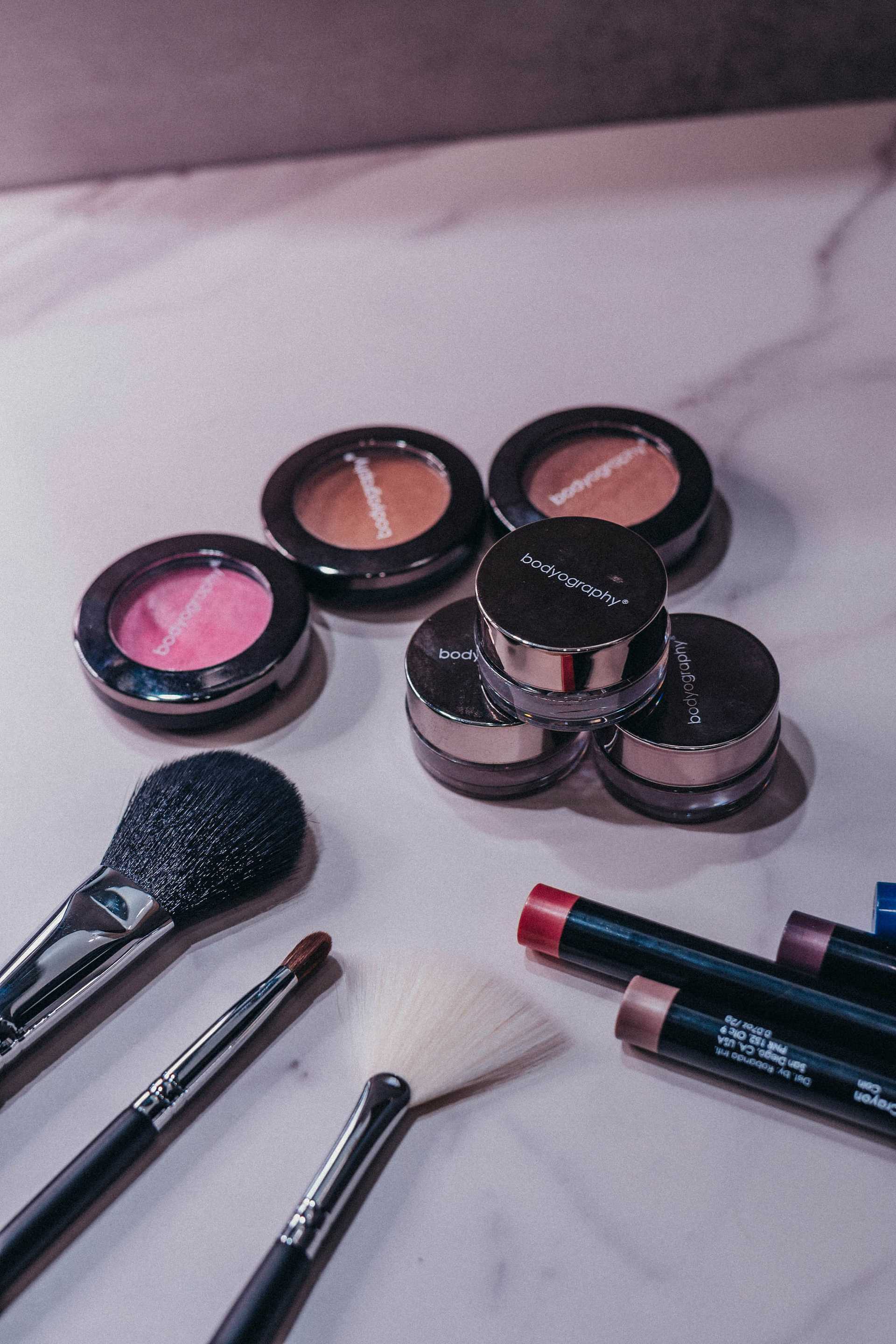 Makeup products with brushes on a marble surface.