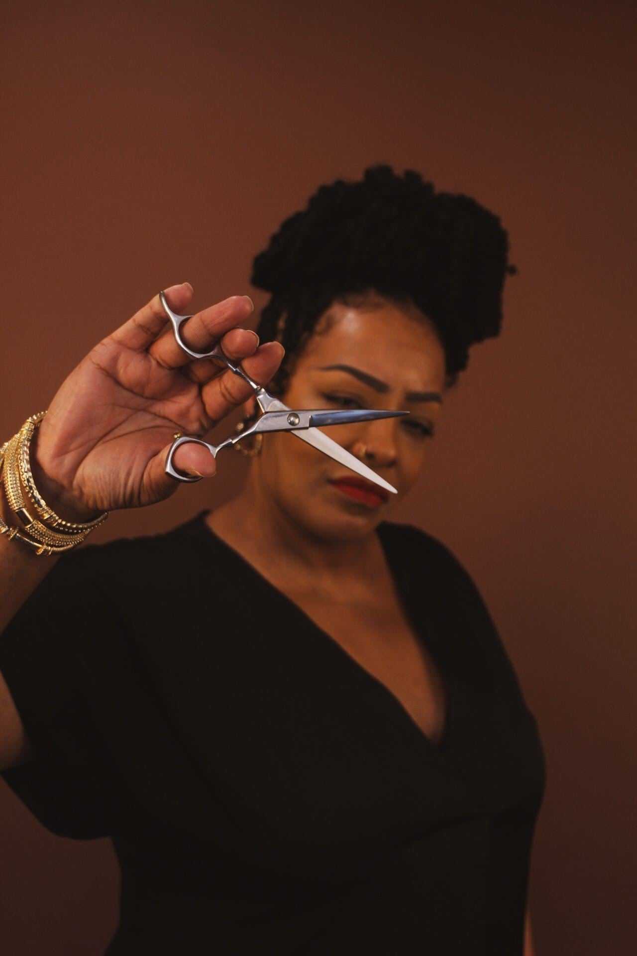 Woman holding scissors against a brown background, focus on the scissors.
