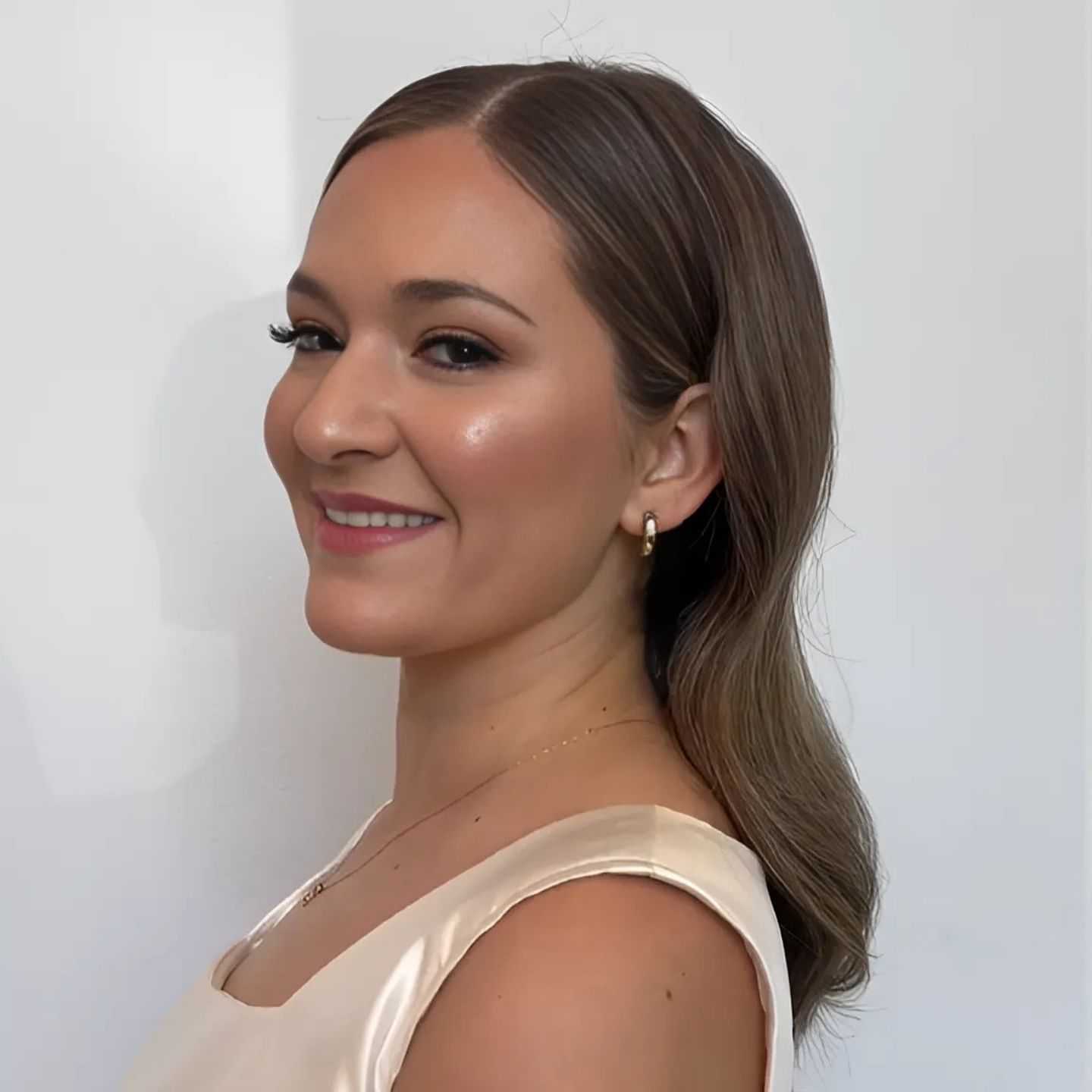 Woman with elegant hairstyle and makeup, smiling and wearing a cream-colored dress.