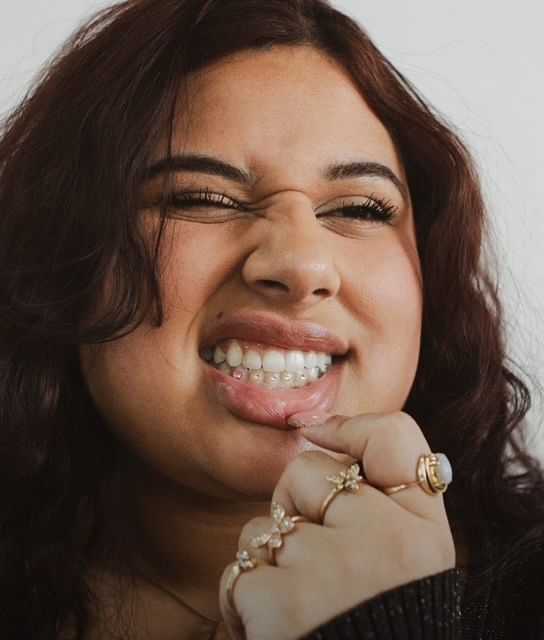 Woman showing her smile with clear braces and wearing multiple rings on her fingers.