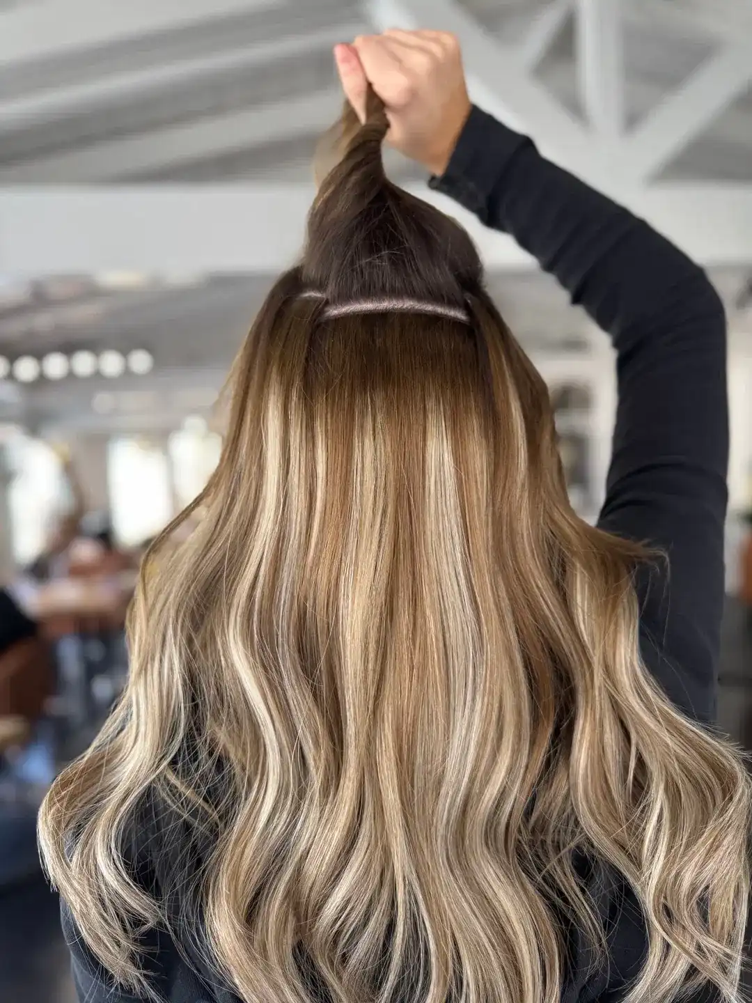 Woman in salon chair getting hair styled with highlights and loose waves.
