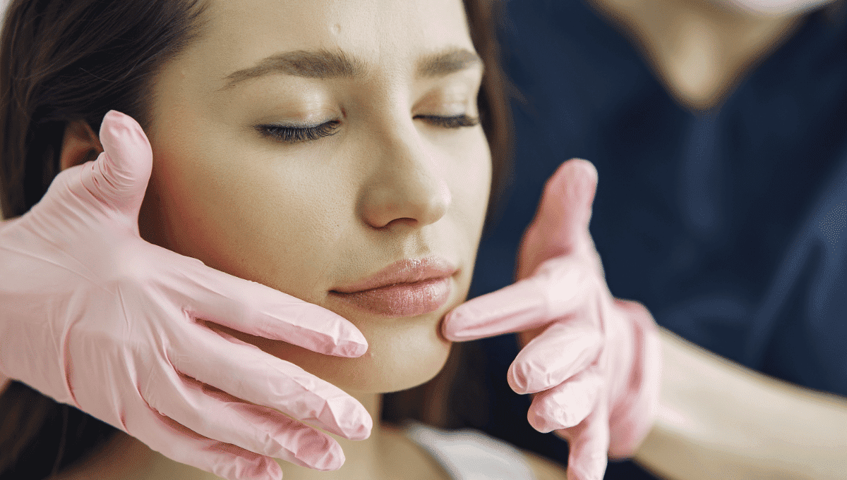 Young woman receiving a facial examination by a professional wearing pink gloves.