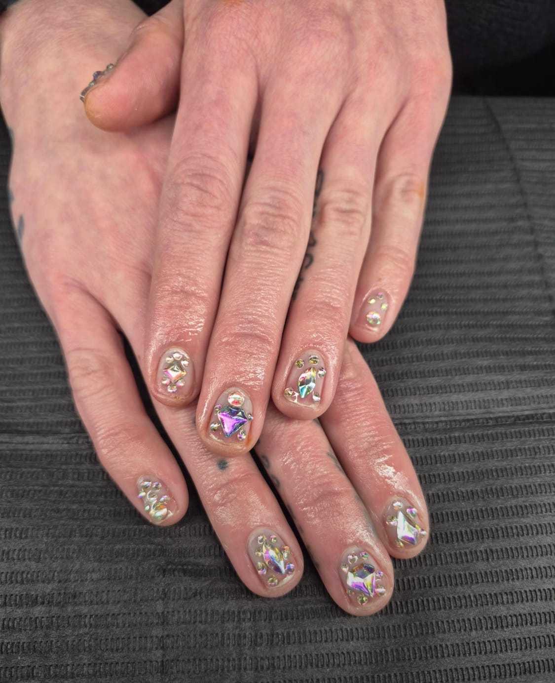 Nails with iridescent gem designs on a textured gray background.