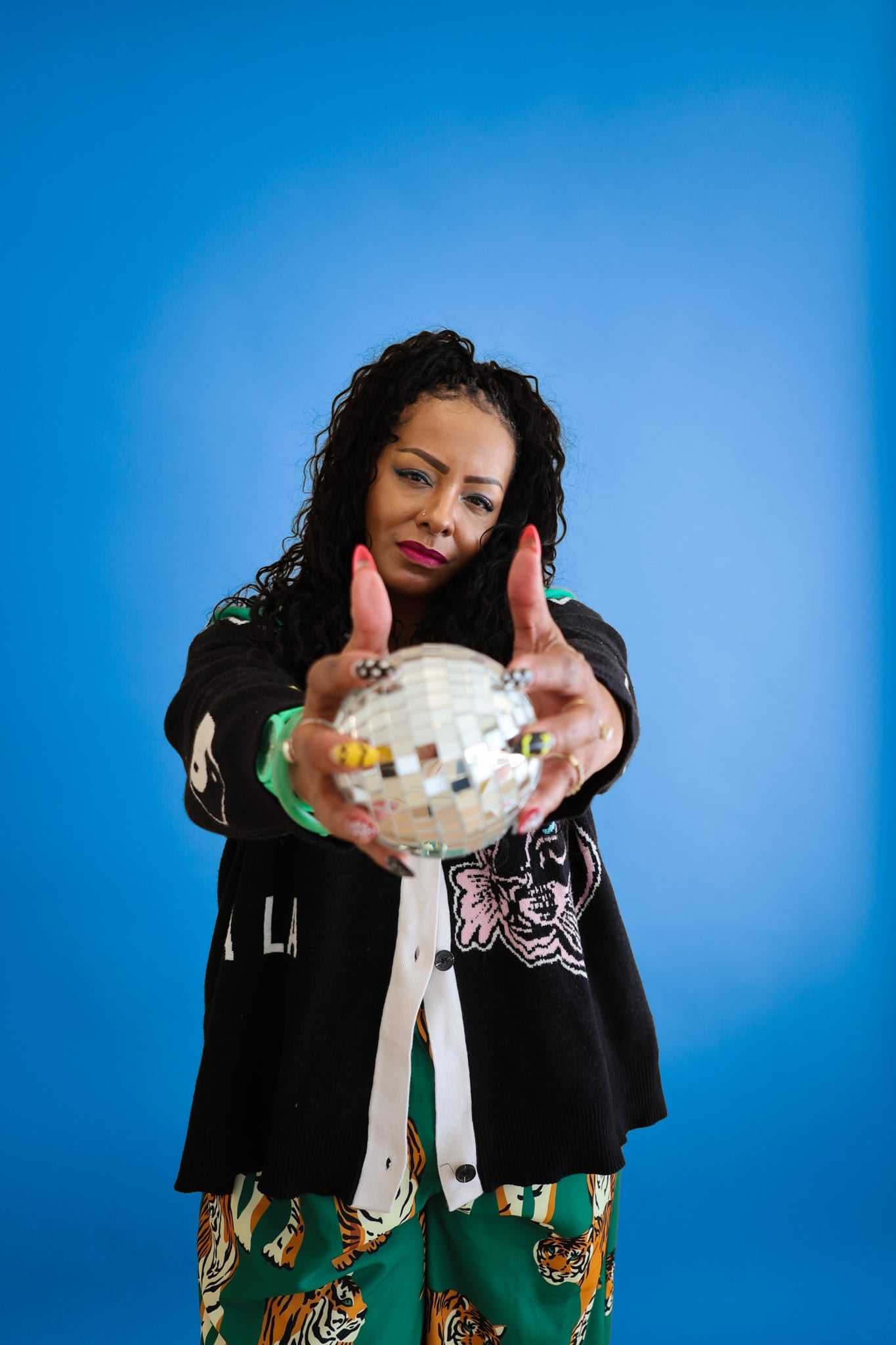 Woman holding a disco ball against a blue background, wearing a patterned outfit.