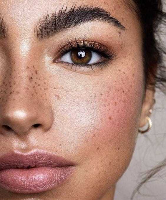 Close-up of a woman's face with freckles, natural makeup, and hoop earrings.