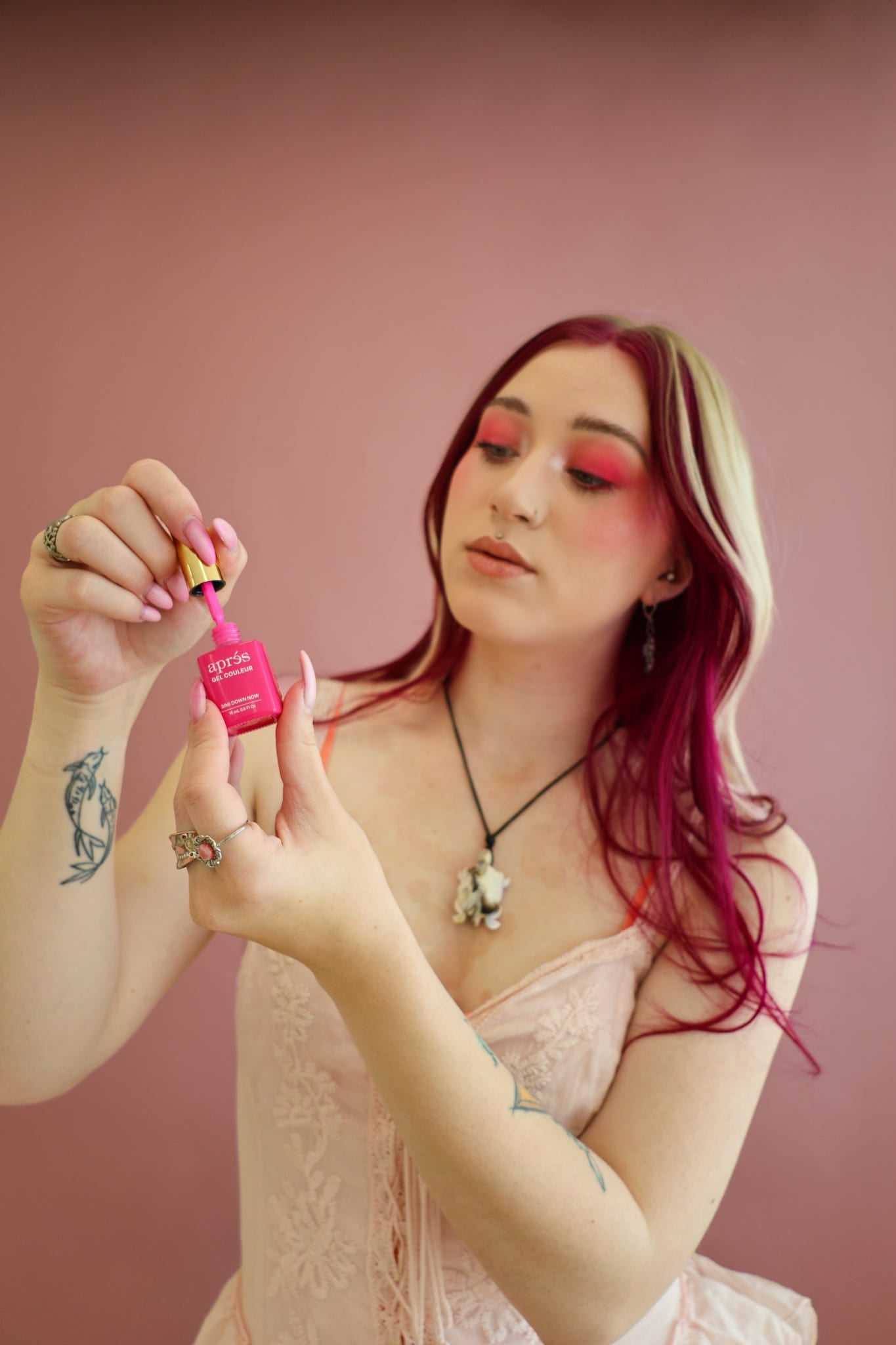Woman holding a pink nail polish bottle against a pink background, showing details.