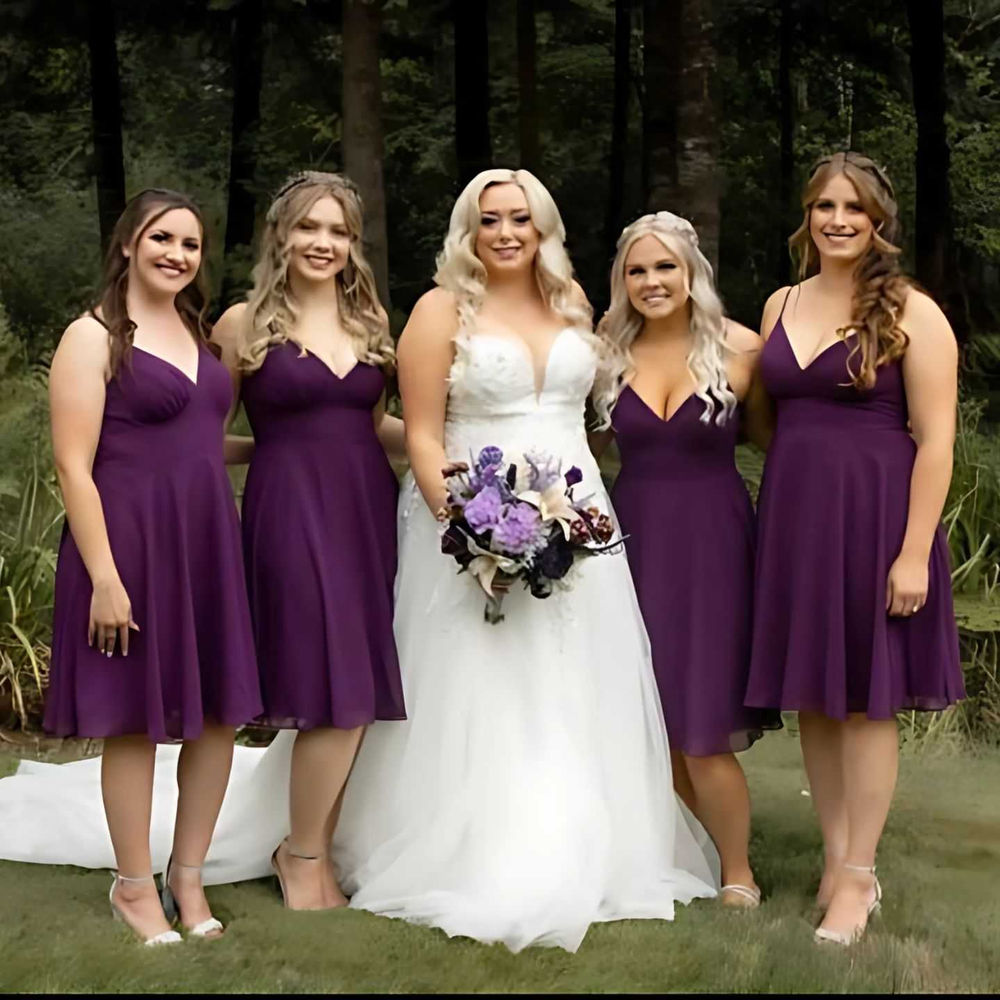 Bride surrounded by bridesmaids in purple dresses, standing in a forested area.