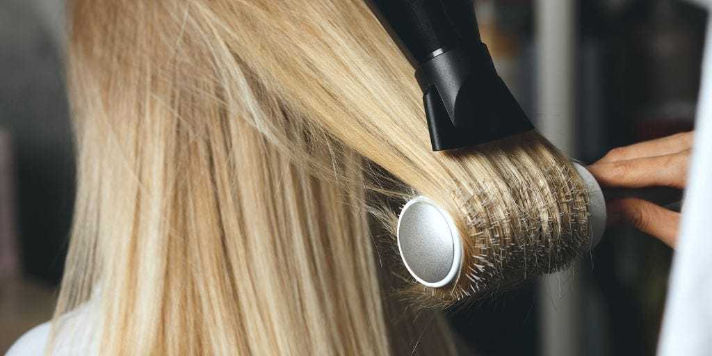Blonde hair being styled with a round brush and blow dryer.