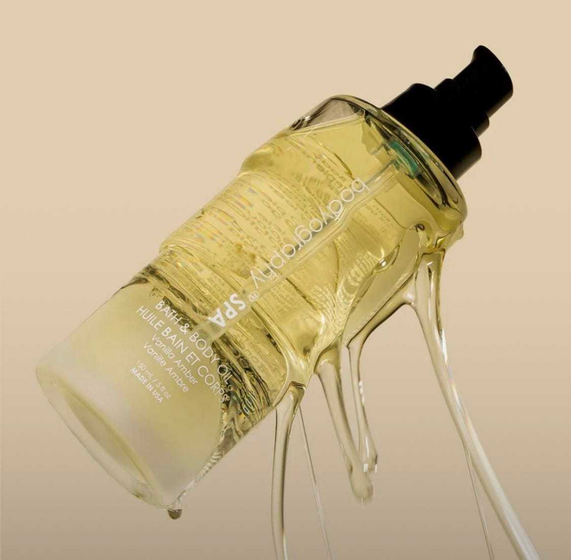 Glass bottle of oil with pump, liquid dripping, beige background.