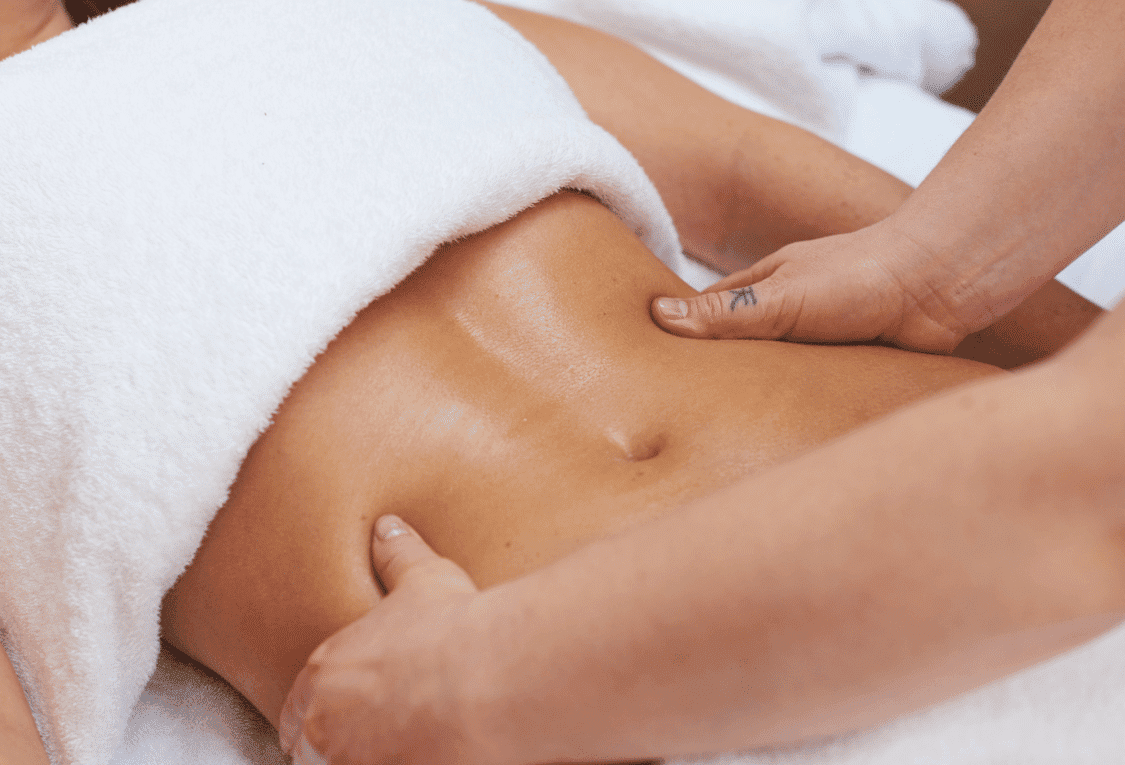 Massage therapist performing abdominal massage on a relaxed person under a white towel.