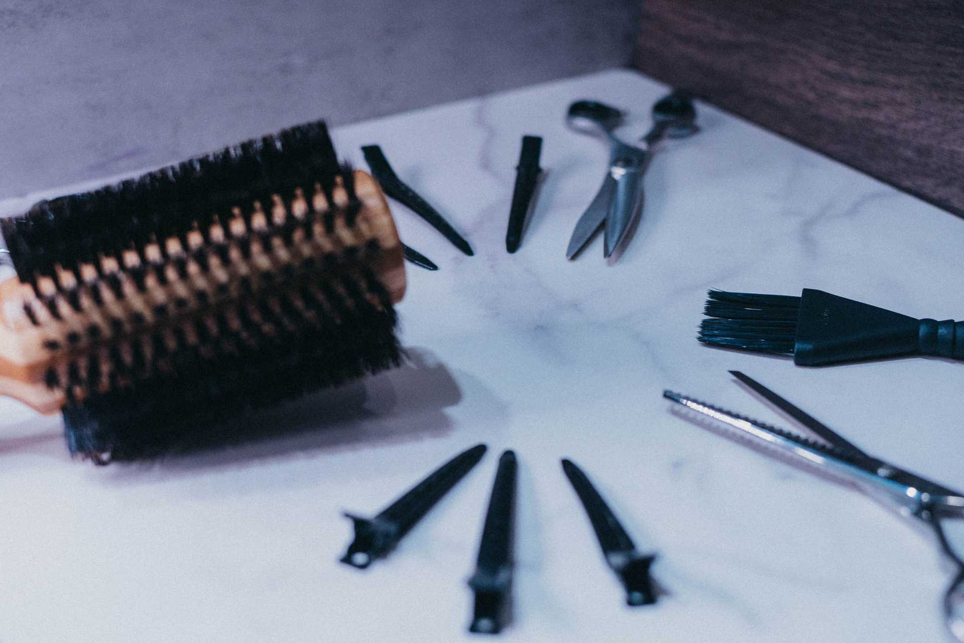 Hairdressing tools on marble: brush, scissors, clips, and comb spread out for styling.