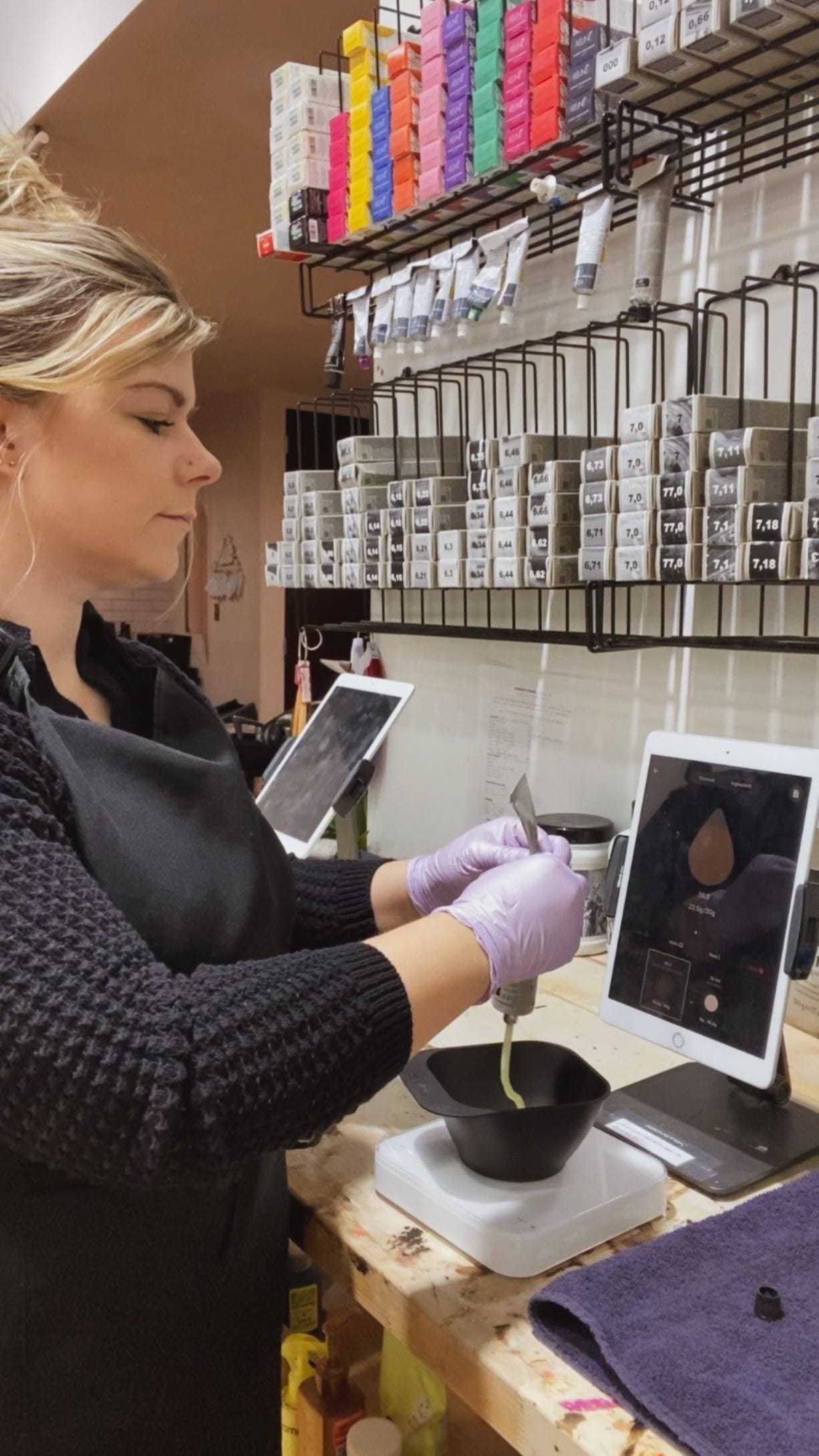 Hairdresser mixing color at a salon work station filled with hair dye products.