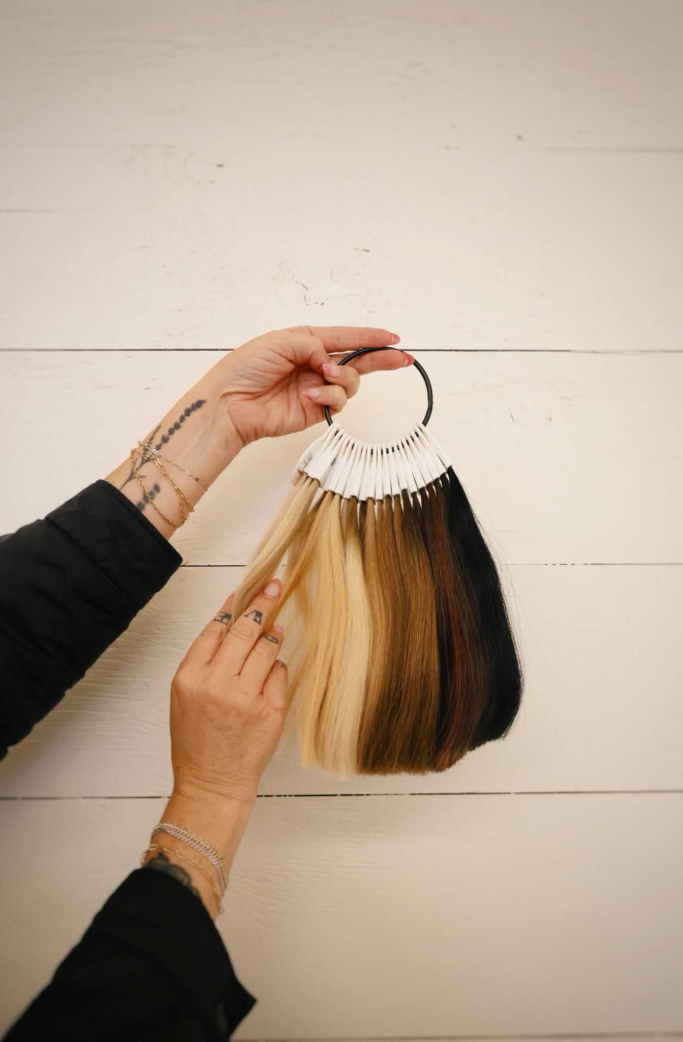 Hair color swatches held by a tattooed hand against a white wooden background.