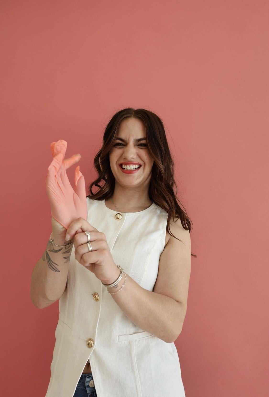 Woman smiling, putting on a pink glove against a pink background.