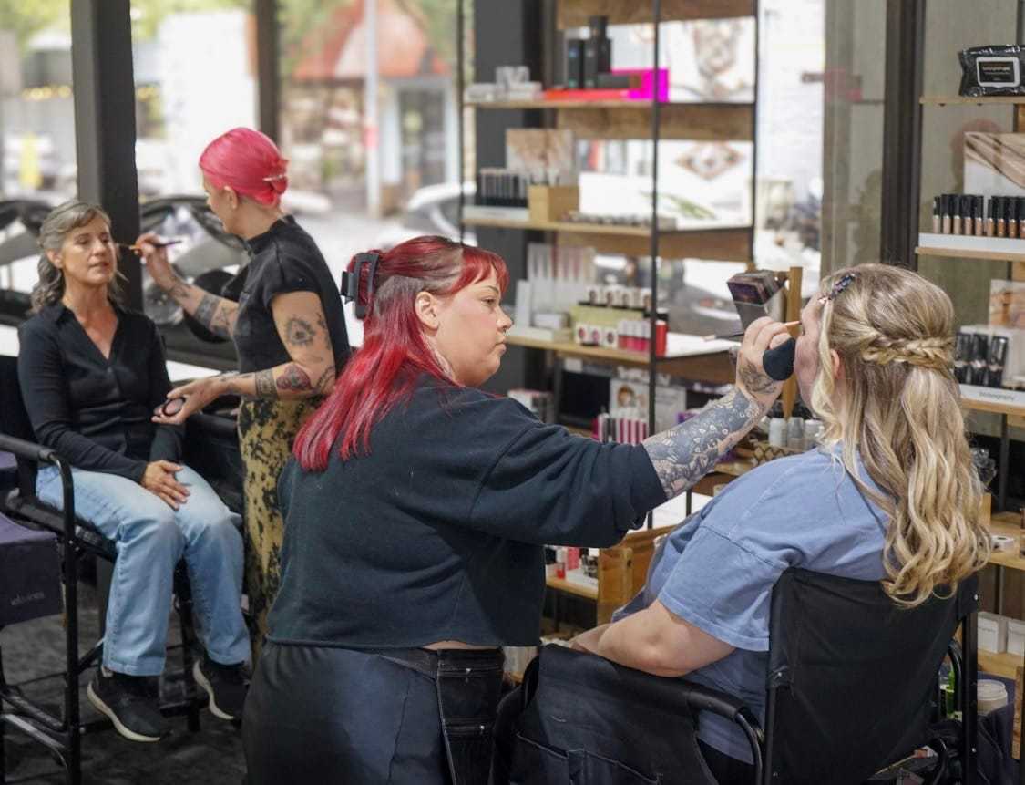 Makeup artists applying makeup to two seated women in a studio.