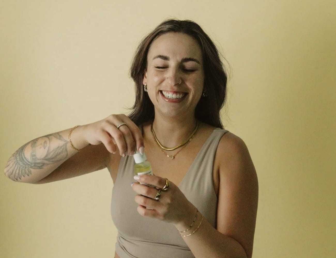 Woman smiling while holding a small bottle against a yellow background.
