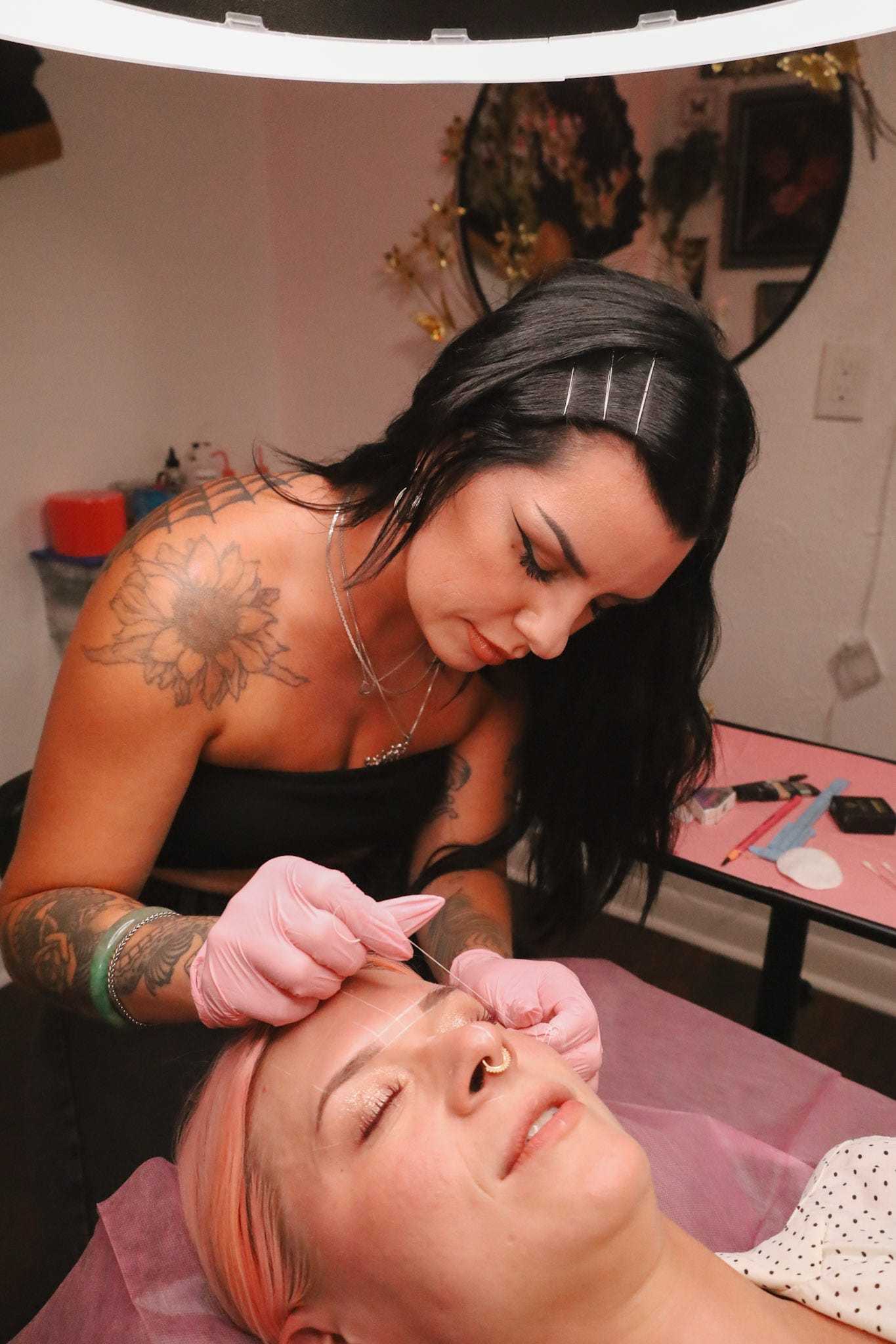 Tattooed artist performing a cosmetic procedure on a reclining client in a salon setting.